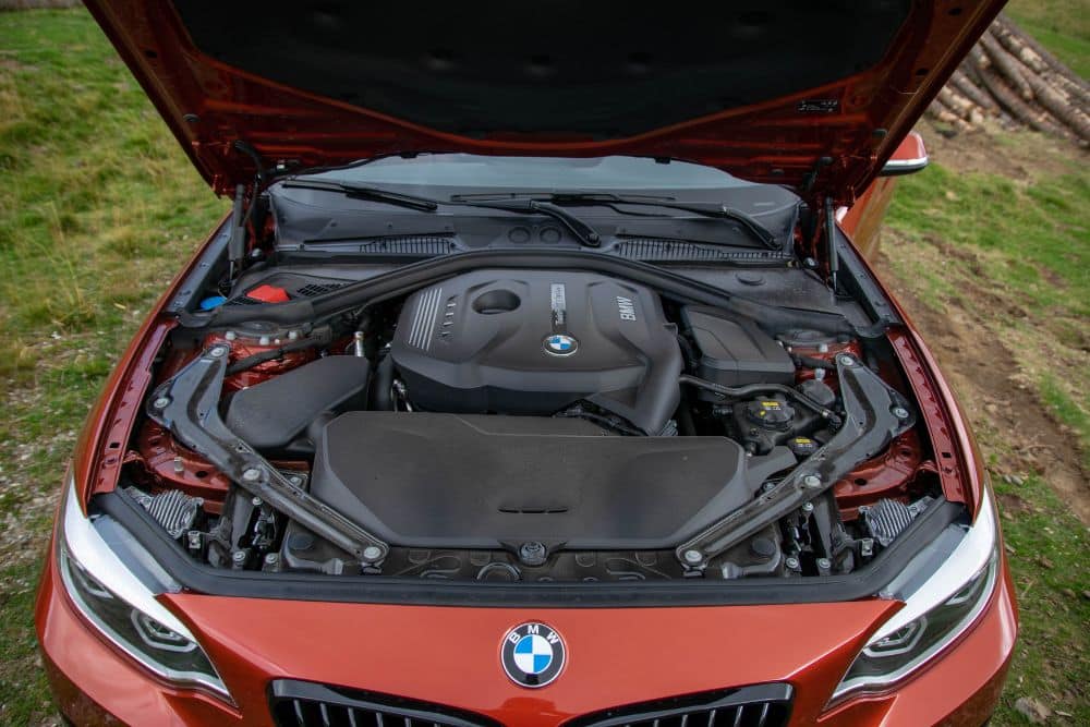 European Car Maintenance auto repair in Mooresville, NC at Rock Solid Autocare. Orange BMW with hood open outdoors, showing a clean engine bay with prominent BMW branding on the engine cover.